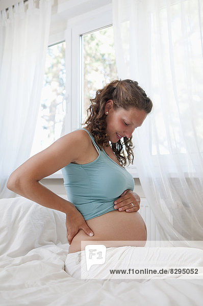 young pregnant woman sitting on bed