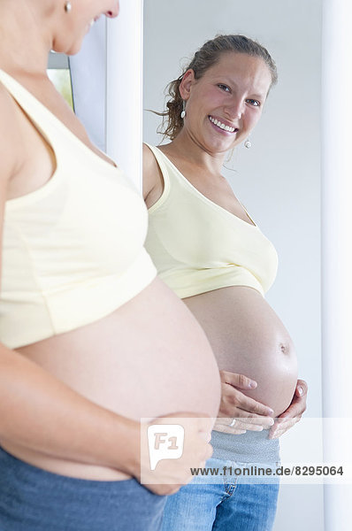 junge schwangere Frau schaut in den Spiegel