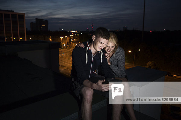 Junges Paar mit Tablett-PC auf dem Flachdach bei Nacht