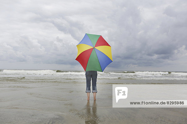 Germany  Lower Saxony  East Frisia  Langeoog  woman with open umbrella standing at the beach