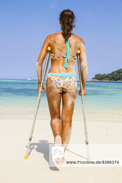 Thailand  Insel Koh Surin  Frau mit Krücken am weissen Sandstrand