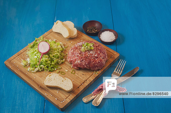 Raw minced meat with spring onions and bread on chopping board,  studio shot