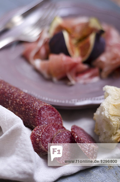 Salami mit Weißbrot  Schinken und Feigen im Hintergrund