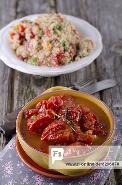 Eingelegte Tomaten mit Knoblauch und Rosmarin  im Hintergrund Couscous-Salat