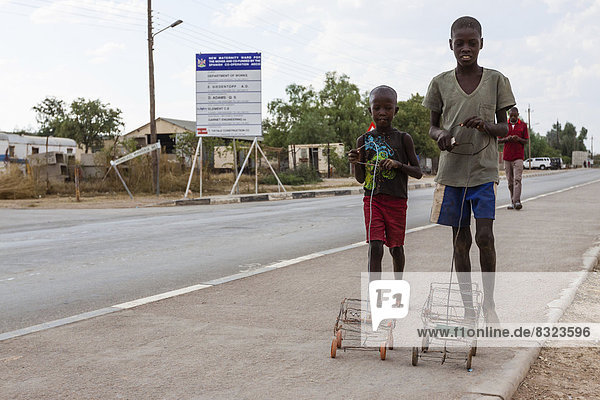 Zwei Himba-Jungen spielen mit ihren selbstgebauten Spielzeugautos am Straßenrand