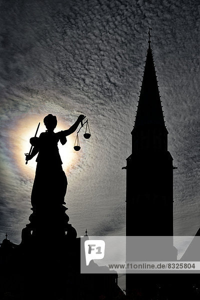 Justitia statue in front of the silhouette of the Old St. Nicholas Church