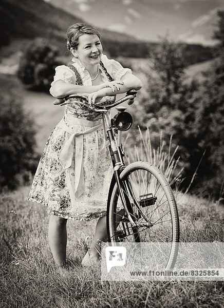 Woman wearing a dirndl with an old bicycle