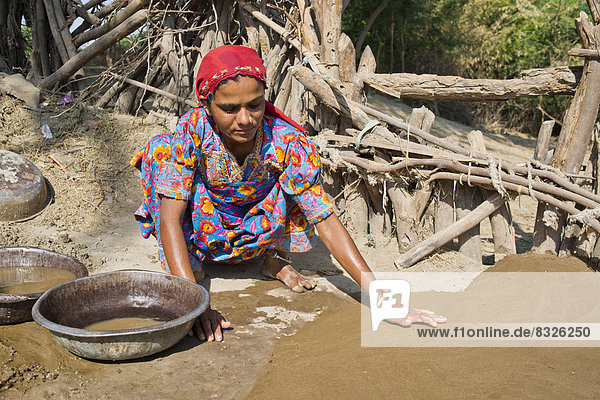 Freundliche junge Frau in traditioneller Kleidung verputzt den Boden eines Innenhofes mit einer Mischung aus Wasser  Sand und Kuhmist