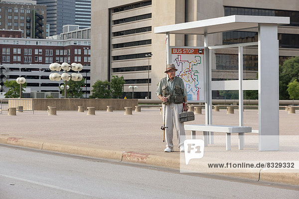 Senior man standing at bus stop with fishing rod
