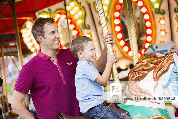 Father and son (4-5) on carousel in amusement park