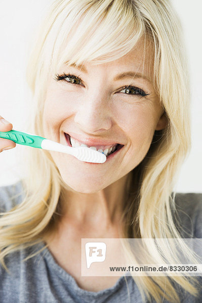 Studio portrait of blonde woman cleaning teeth