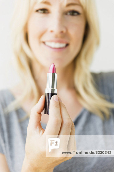Studio portrait of blonde woman holding pink lipstick