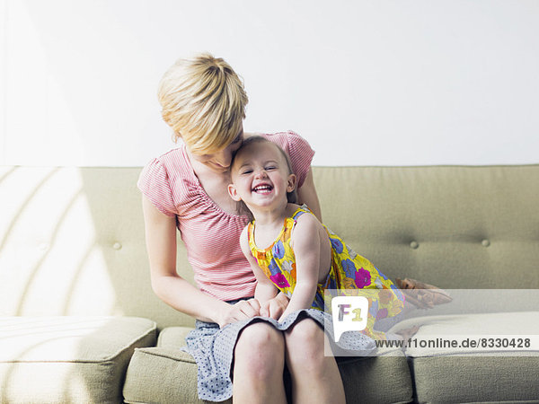Mother with daughter (12-17 months) sitting on sofa