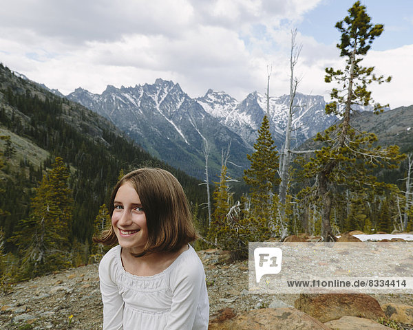 Ein junges Mädchen sitzt an einem Aussichtspunkt mit Blick auf die Berge des Wenatchee-Nationalwaldes.