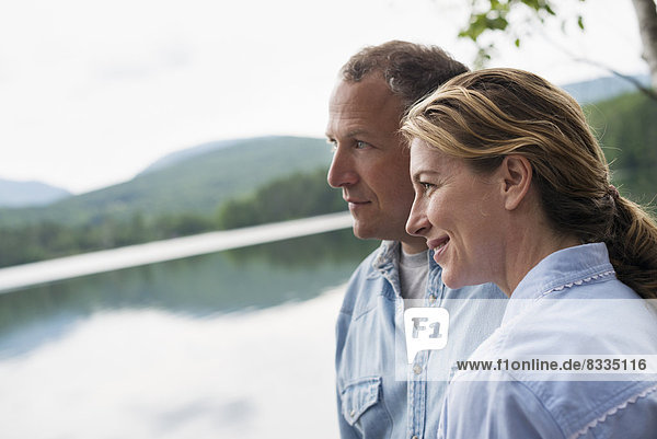 A mature couple standing by a lake shore.