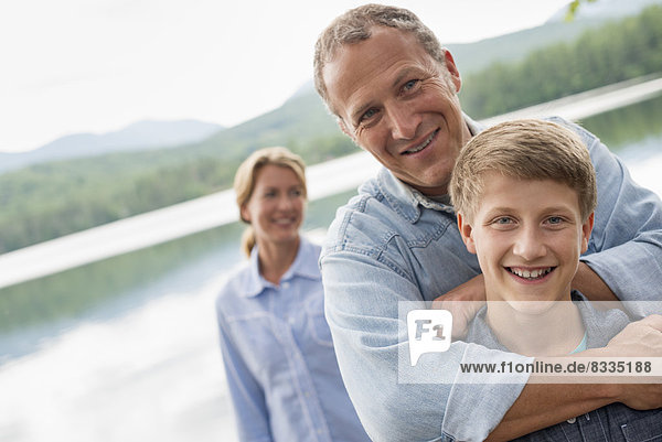 A family outdoors under the trees on a lake shore. Two adults and a young boy.