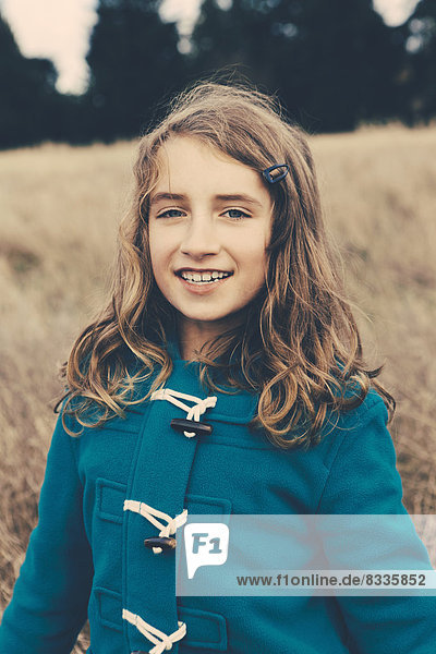 Ein junges neunjähriges Mädchen in einem blauen Seesackmantel  das in die Kamera lächelt.