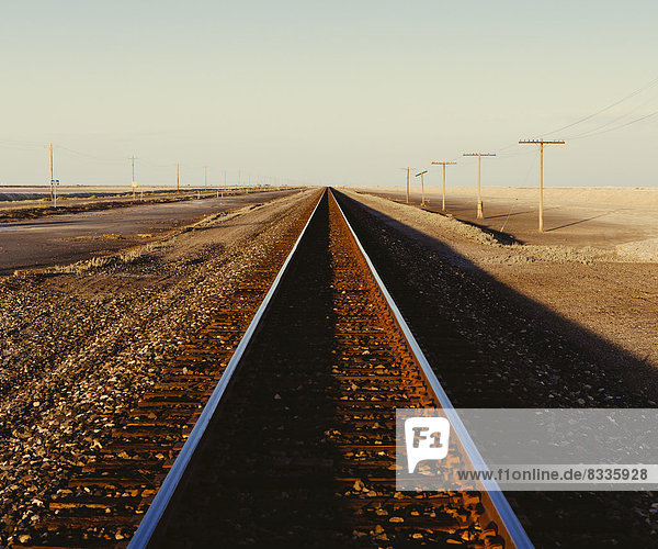 Eisenbahnschienen  die in der Abenddämmerung durch die flache Wüstenlandschaft Utahs führen.