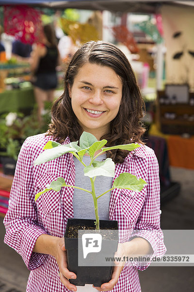 A young woman holding a small plant in a pot. Farm stand.
