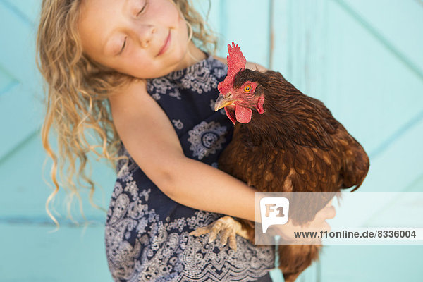 A young girl holding a chicken in her arms.