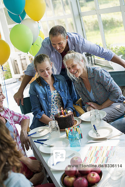 Eine Geburtstagsfeier in einer Bauernküche. Eine Gruppe von Erwachsenen und Kindern versammelte sich um einen Schokoladenkuchen.