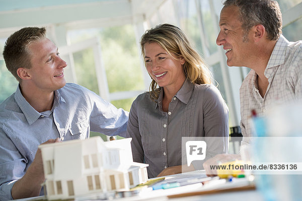 A farmhouse kitchen. A model of a house on the table. Planning and designing a house build. Three people.