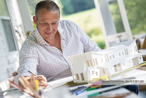Eine Bauernhaus-Küche. Ein Modell eines Hauses auf dem Tisch. Ein Haus entwerfen. Ein Mann mit einer Bleistiftzeichnung auf einem Plan.