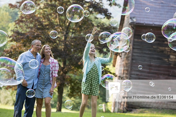 A family sitting on the grass outside a bar  blowing bubbles and laughing.