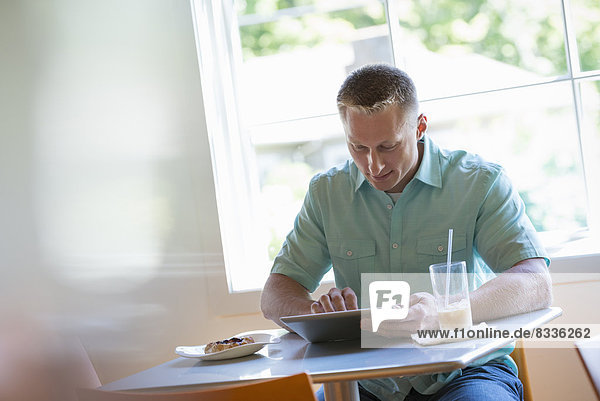 Ein Mann mit kurz geschnittenem Haar sitzt an einem Café-Tisch. Er benutzt ein digitales Tablett.