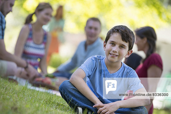 Eine Gruppe von Erwachsenen und Kindern sitzt auf dem Gras im Schatten eines Baumes. Eine Familienfeier.
