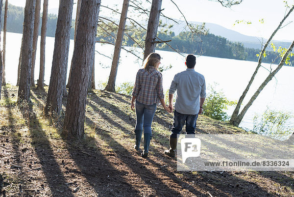 A couple walking in woodland on the shores of a lake.