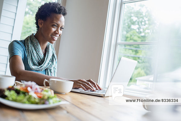 A woman sitting in a cafe with a cup of coffee and a meal. Using a laptop.