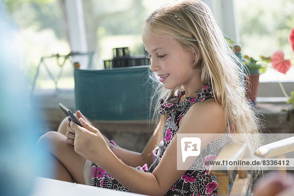A young girl in a flowered dress using a digital tablet. Sitting at a table.