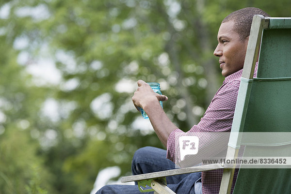 Ein Mann sitzt auf einem Stuhl in einem Garten und entspannt sich.