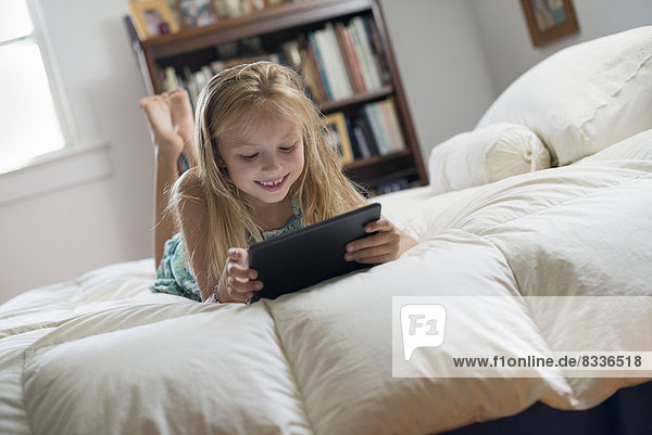 A young girl sitting on her bed using a digital tablet.