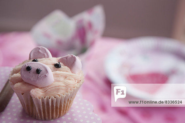 Ein Geburtstagstisch mit einem rosa Tuch und einem mit dem Bild eines Schweins dekorierten Kuchens.