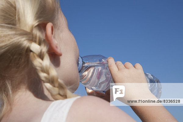Ein kleines Kind mit blonden Haaren in Zöpfen  das Wasser aus einer durchsichtigen Flasche trinkt.