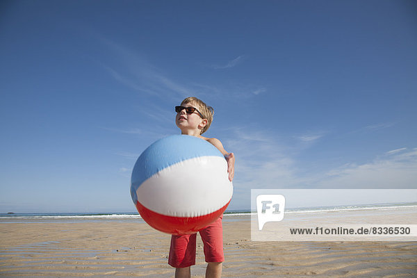 Ein Junge am Strand  der einen großen aufblasbaren Strandball hält.