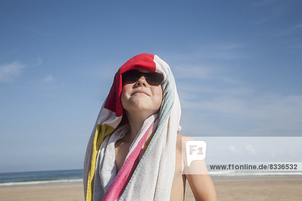 Ein Junge mit Sonnenbrille und einem Handtuch über dem Kopf.