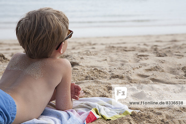 Ein Junge liegt vorne auf dem Sand und schaut aufs Meer hinaus.
