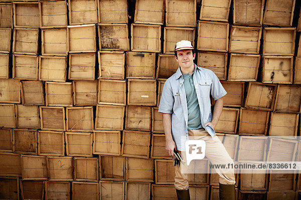 Ein Landwirt steht vor einer Wand aus gestapelten Holzkisten für die Produktion.
