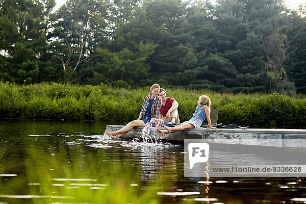 Drei Personen  zwei Erwachsene und ein Kind  die sich auf einem Steg entspannen  mit den Füßen im Wasser am Ende eines Tages.