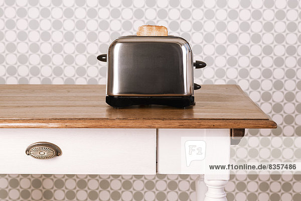 Alter Küchentisch mit Toaster und Brotscheibe vor Ziertapete,  Studioaufnahme