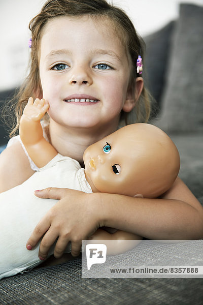Porträt eines lächelnden kleinen Mädchens auf dem Sofa mit ihrer Puppe  Nahaufnahme