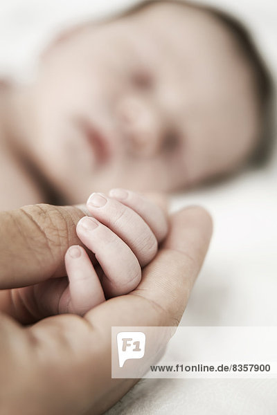 Vater hält die Hand seines schlafenden neugeborenen Sohnes