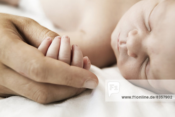 Mother holding hand of her sleeping newborn son