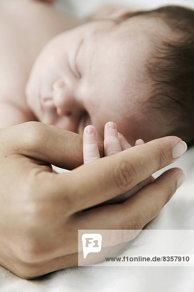 Mutter hält die Hand ihres schlafenden  neugeborenen Sohnes.