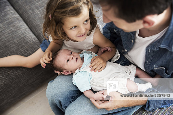 Junger Vater mit männlichem Neugeborenen und kleiner Tochter  die zu Hause auf dem Sofa sitzt.