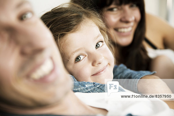 Young parents with little daughter sitting on sofa at home  close-up