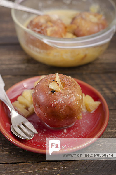 Baked apples with almonds  gloves and cinnamon in glass bowl and red plate on wooden table  studio shot